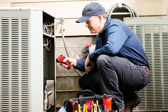 Technician inspecting an outdoor HVAC unit with tools while performing system diagnostics.