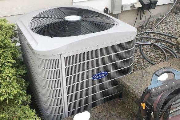 Carrier outdoor air conditioning unit installed beside a home with tools nearby.